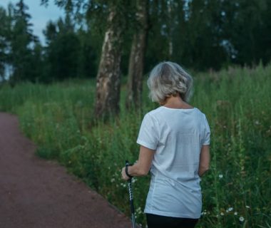 Elderly woman practicing Nordic walking on a park trail, promoting health and fitness.